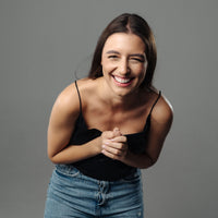 Thumbnail for Smiling woman in a black top and jeans, radiating joy and happiness, with a grey background.