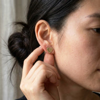 Thumbnail for Heart Initial Stud Earrings in Gold held between the fingertips, scale reference | SKU: heart-initial-gold-a