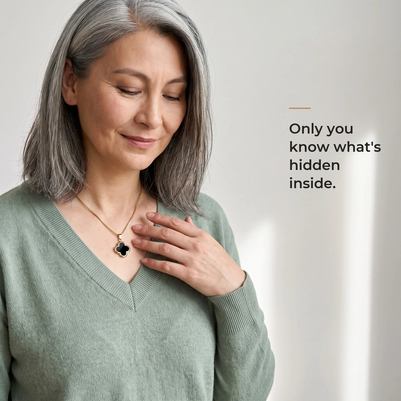Grey-haired woman in a sage sweater touching the black clover pendant on its gold chain, only she knows the photo inside | SKU: TPH-CLVN-GOLD